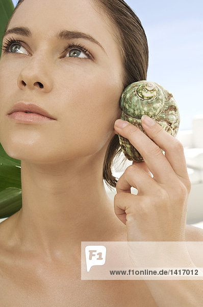 Portrait of a young woman holding a shell against her ear  outdoors