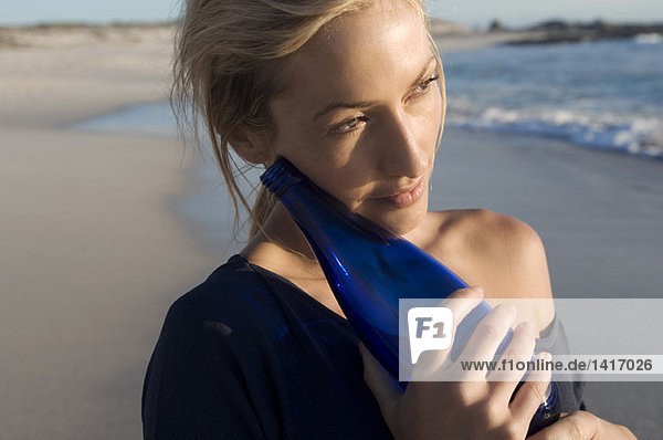 Portrait of a young woman on the beach  holding a bottle  outdoors