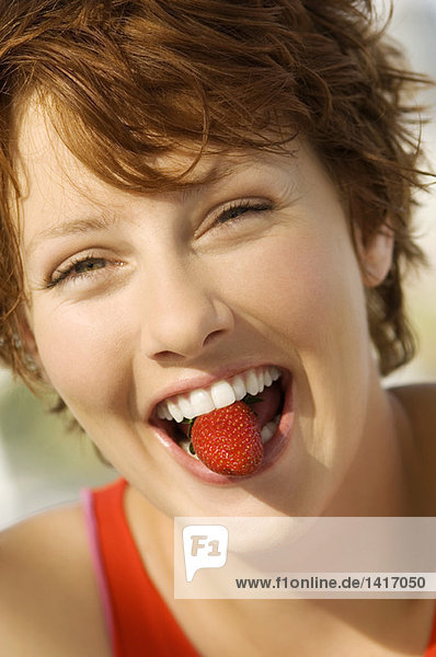 Porträt einer jungen Frau mit Erdbeere zwischen den Zähnen