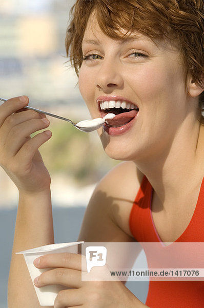 Portrait of a young smiling woman eating yogurt