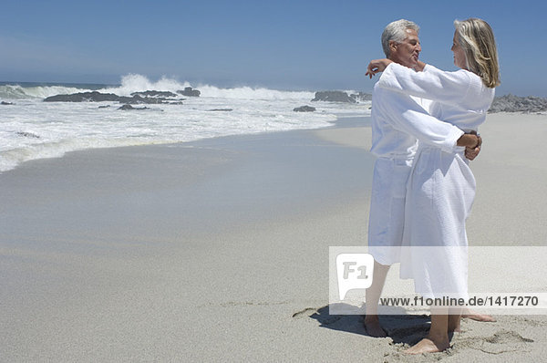 Paar im Bademantel  am Strand umarmend