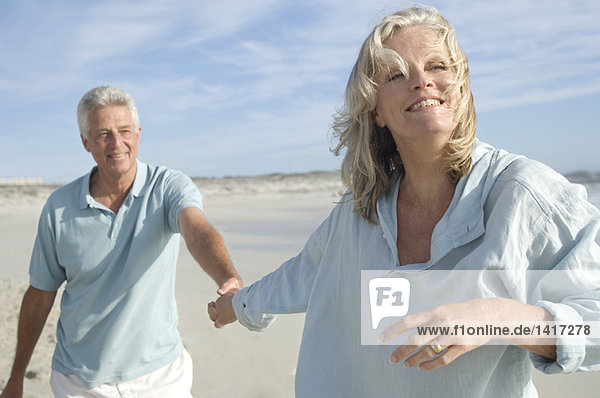Ein Paar hält sich an den Händen und geht am Strand spazieren.