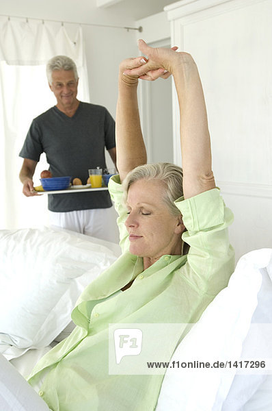 Man bringing breakfast to woman stretching in bed