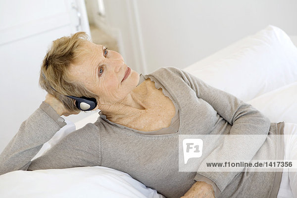 Senior woman lying on bed  listening to music with headphones
