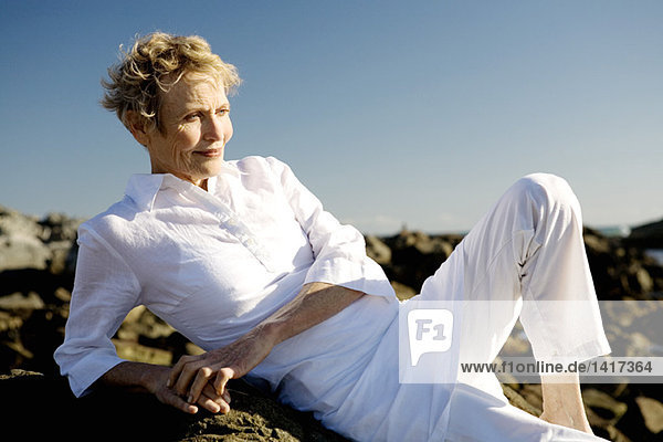 Senior woman lying on seaside rocks