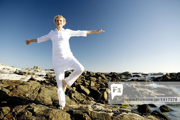 Senior woman doing yoga on seaside rocks