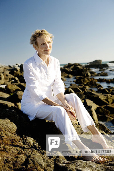 Senior woman sitting on seaside rocks