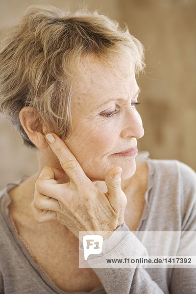 Porträt einer älteren Frau  die ihr Ohr berührt.