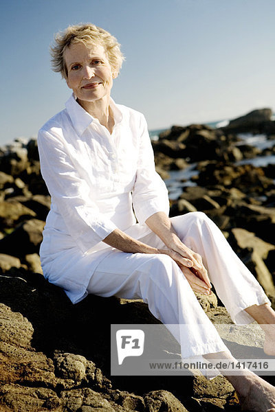 Seniorin auf Felsen am Meer sitzend