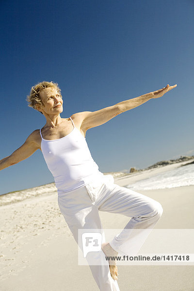 Seniorin beim Yoga am Strand