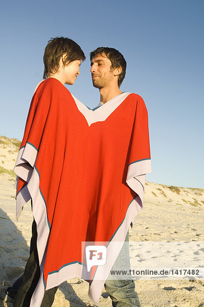 Ein Paar am Strand  das sich einen Poncho teilt.