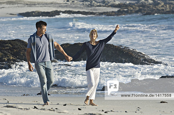 Ein Paar hält sich an den Händen und geht am Strand spazieren.