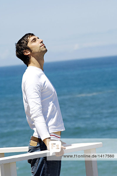 Young man leaning against balustrade  eyes closed  sea in background