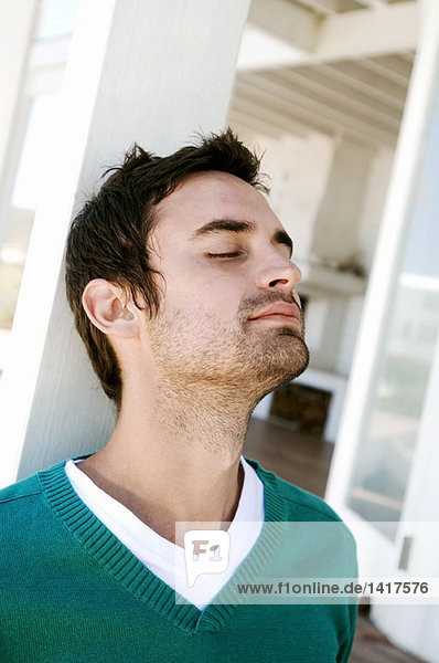 Portrait of a young man with eyes closed  leaning against terrace beam