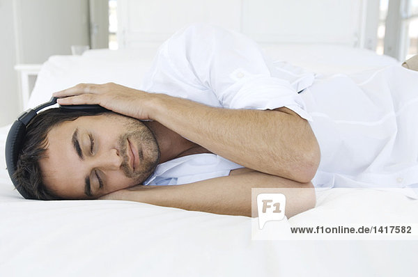 Young man listening to music with headphones  lying on bed
