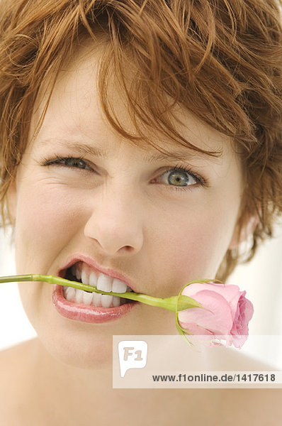 Porträt einer jungen Frau mit Rose zwischen den Zähnen