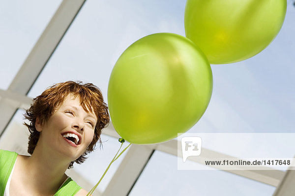 Porträt einer jungen lächelnden Frau mit grünen Luftballons