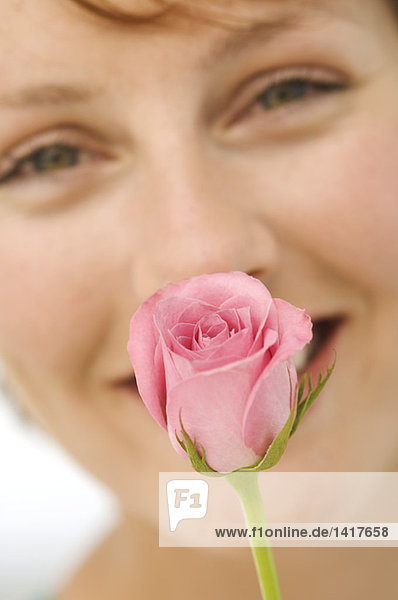 Porträt einer jungen lächelnden Frau mit Rose vor dem Gesicht