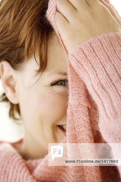 Portrait einer jungen Frau  die ihr Gesicht mit einem Pullover bedeckt.