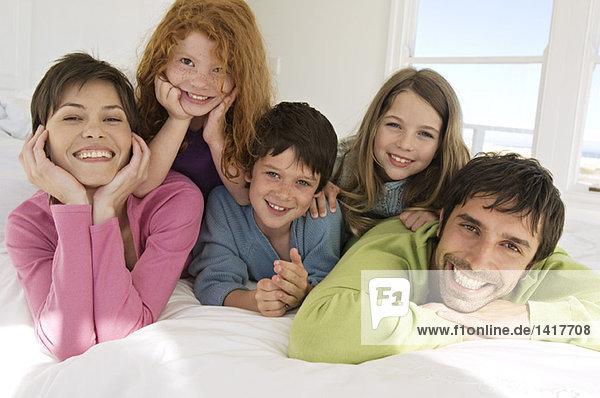 Lächelndes Paar mit 3 Kindern auf dem Bett liegend
