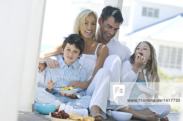 Couple and two children eating  sitting on wooden terrace