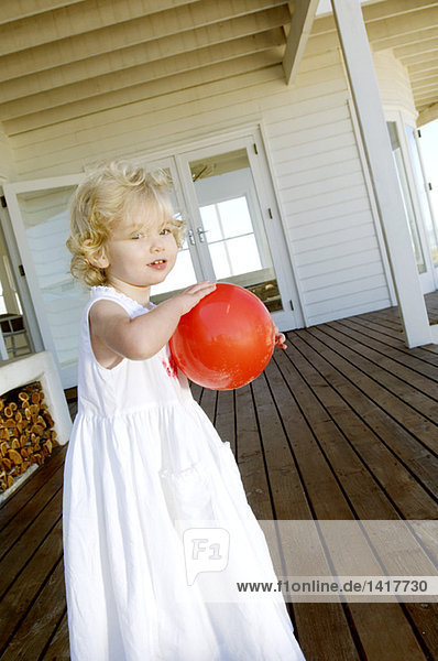 Kleines Mädchen mit rotem Ball auf Holzterrasse