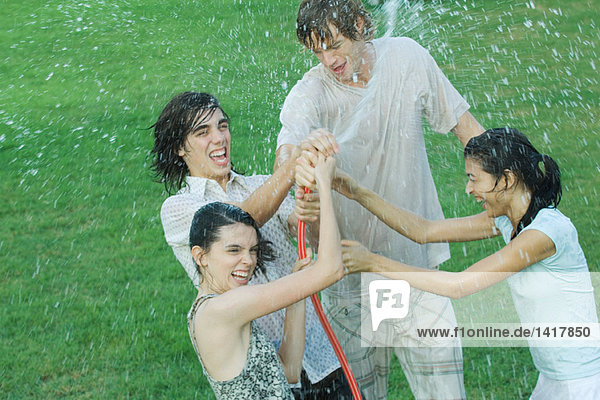 Gruppe junger Freunde  die mit Gartenschlauch spielen  nass werden