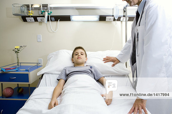 Junge im Krankenhausbett liegend  Arzt neben ihm stehend