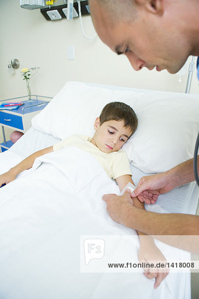 Junge liegt im Krankenhausbett  während der Arzt den Arm des Jungen bandagiert.