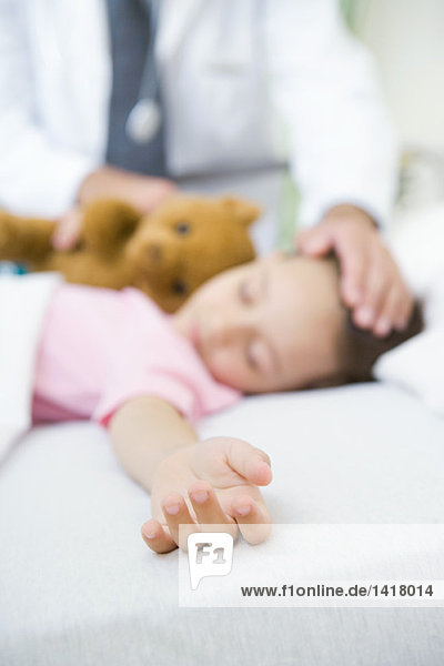 Mädchen schläft im Krankenhausbett  Arzthand auf der Stirn