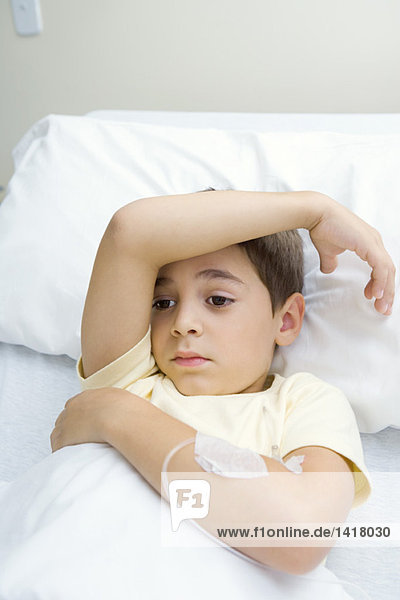Junge im Krankenhausbett liegend mit Arm über der Stirn  wegschauend