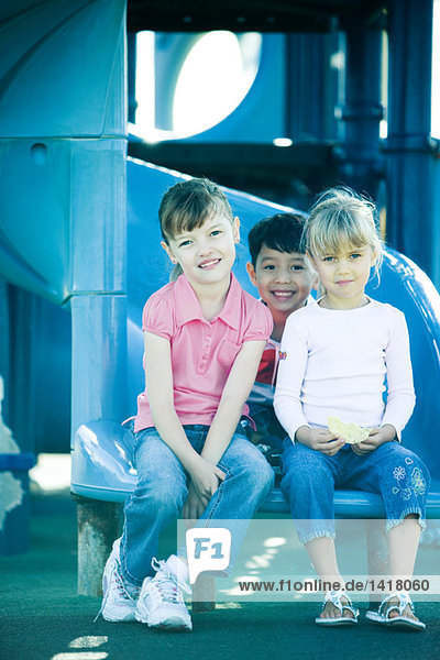 Kinder sitzen auf der Rutsche und lächeln in die Kamera.