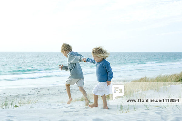 Schwester und Bruder halten Händchen am Strand