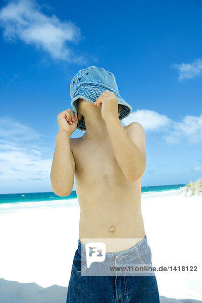 Junge zieht Hut über Gesicht am Strand herunter