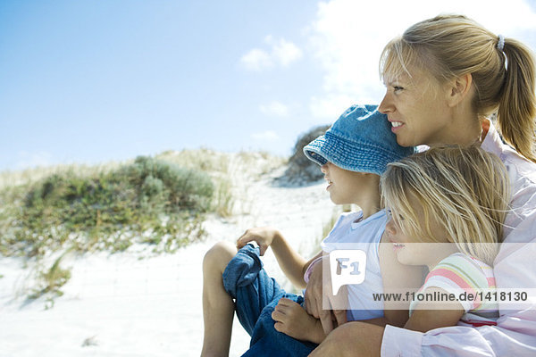 Frau mit Sohn und Tochter auf dem Schoß  Blick in die Ferne  Düne im Hintergrund