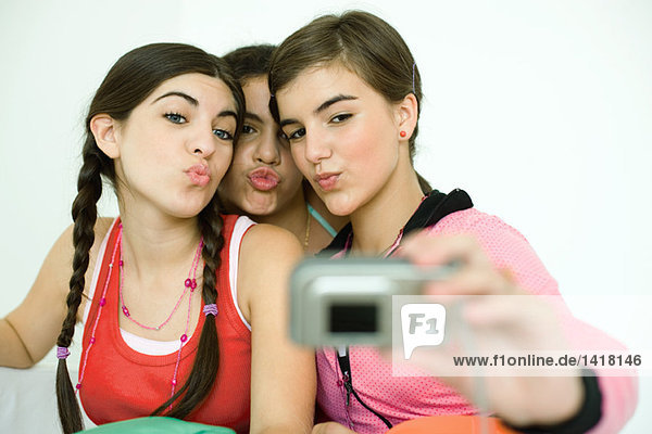 Three young female friends puckering as one takes photo with digital camera