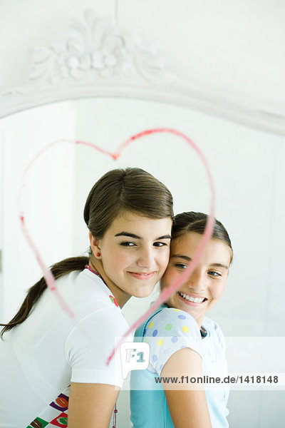 Two young female friends  reflected in mirror with heart drawn in lipstick