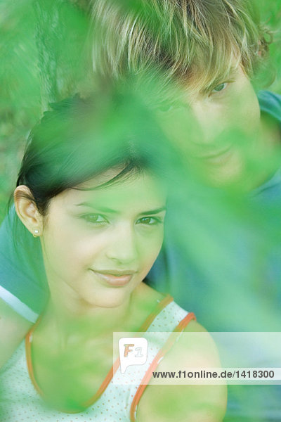 Junges Paar  lächelnd in die Kamera  Portrait  grüne Unschärfe im Vordergrund