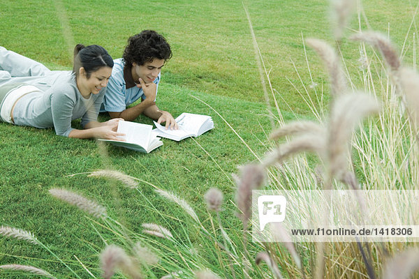 Junges erwachsenes Paar beim Lesen im Freien  auf Gras liegend