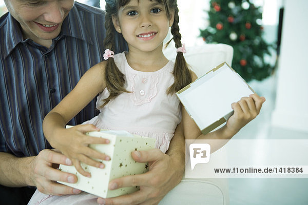 Mädchen auf Vaters Schoß sitzend mit Weihnachtsgeschenk