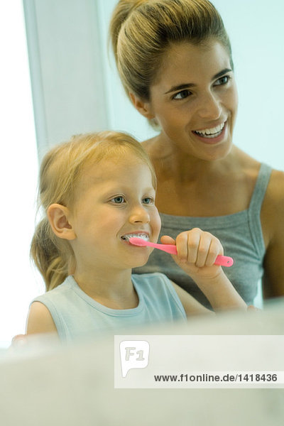 Mutter und Tochter zusammen  während das Mädchen die Zähne putzt.