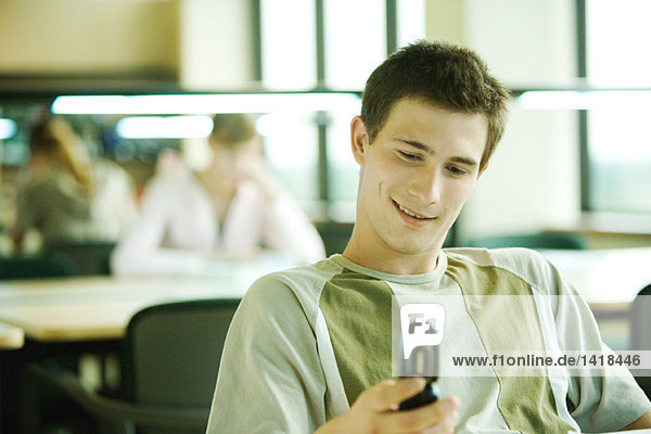 Männlicher Student sitzt im Studienzimmer  schaut auf das Handy  lächelt