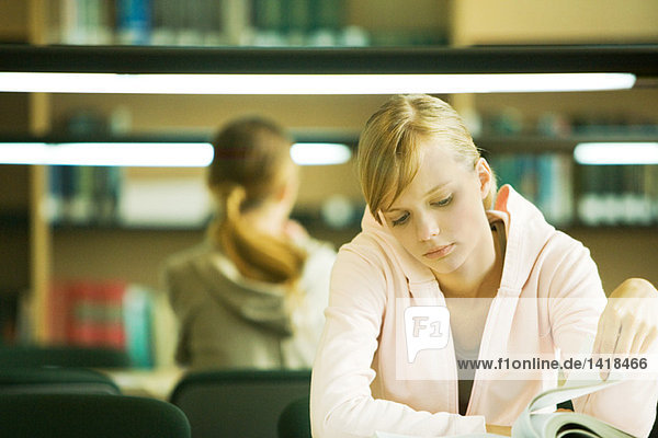 Studentin sitzt am Tisch in der Bibliothek und studiert