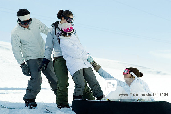 Mädchen sitzt auf dem Boden  auf dem Snowboard  wird von Freunden hochgezogen.