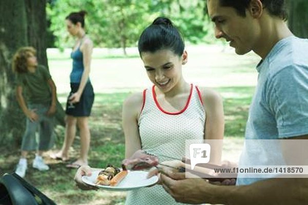 Mann serviert Teenager-Mädchen gegrilltes Fleisch vom Grill