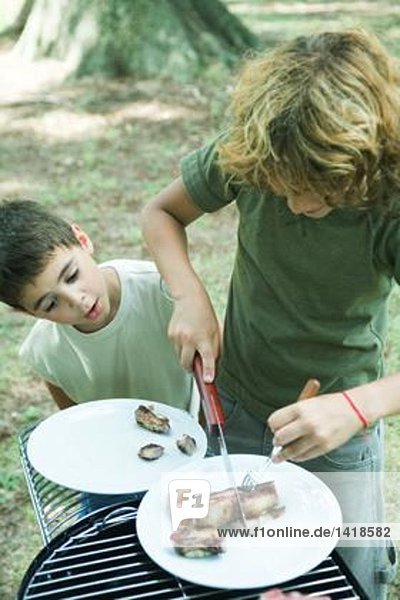 Junge schneidet Fleisch auf dem Teller  während der zweite Junge zusieht.