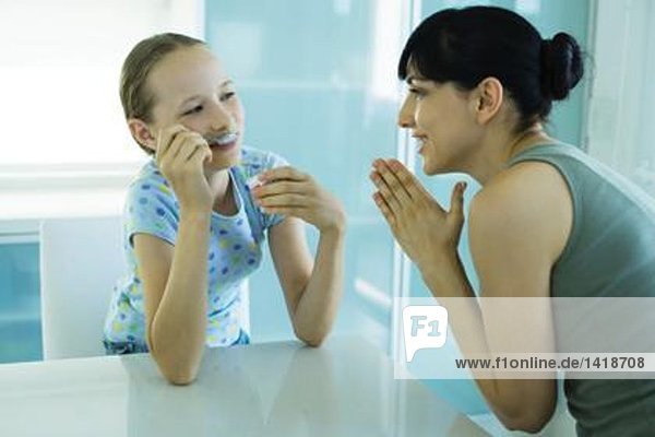 Mädchen isst Eisdessert  Frau schaut Mädchen mit umklammerten Händen an