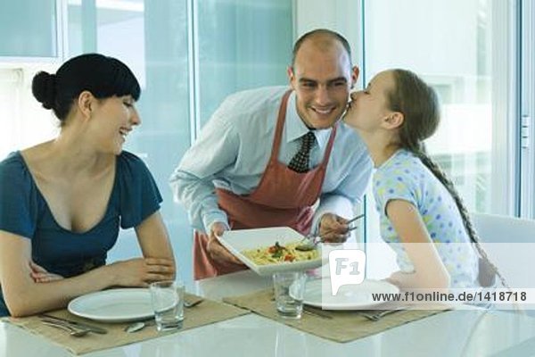 Mann serviert Frau und Tochter Spaghetti  Mädchen küsst Vater auf Wange