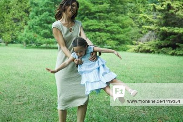 Frau schwingt kleines Mädchen auf Gras herum