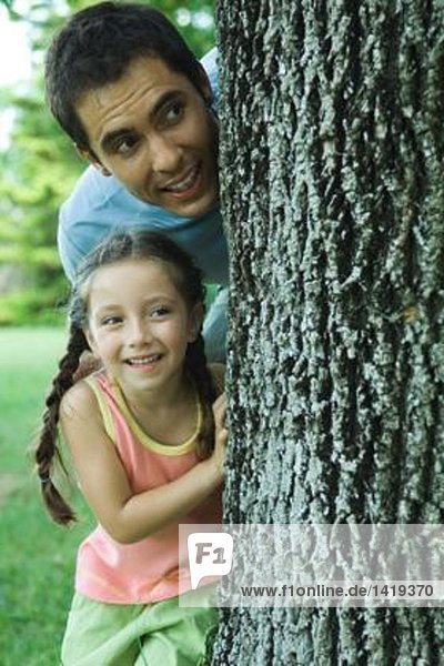 Mädchen und Vater schauen um den Baum herum